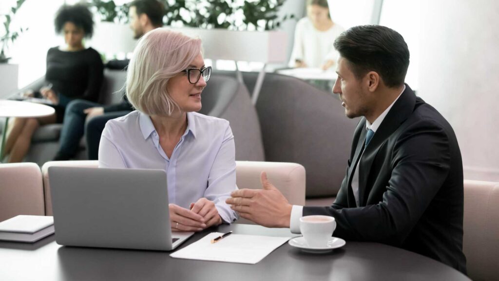 Two professionals discussing work over a laptop in a bright office