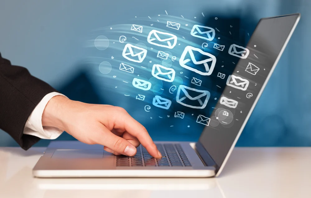 Hand on a laptop with email icons flying from the screen