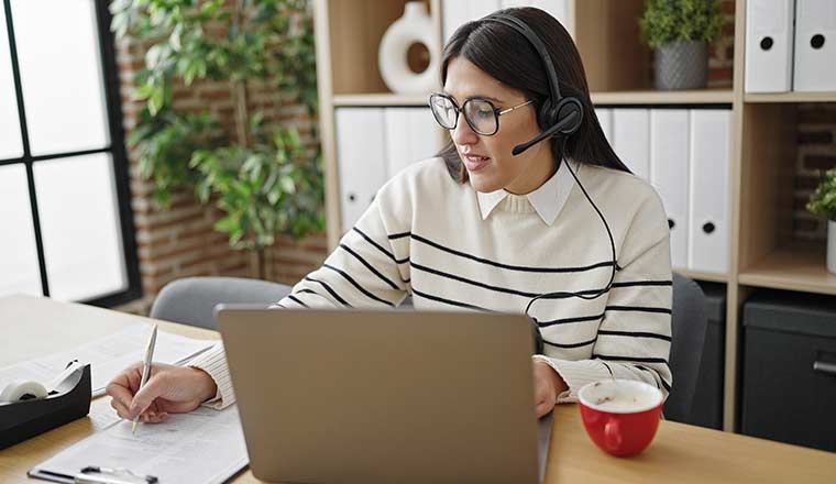 Woman with a headset taking notes at a laptop