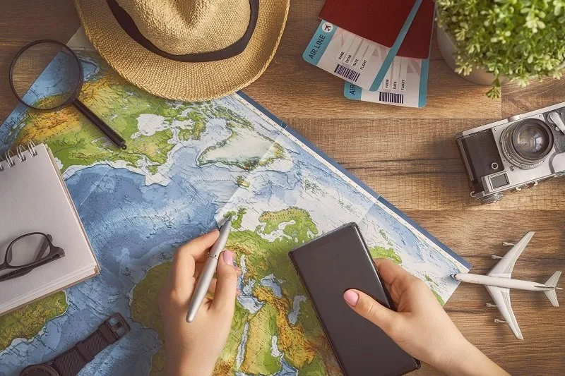 Travel planning flat lay with a map, sun hat, camera and passport